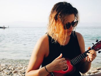 Woman playing guitar at beach against sky