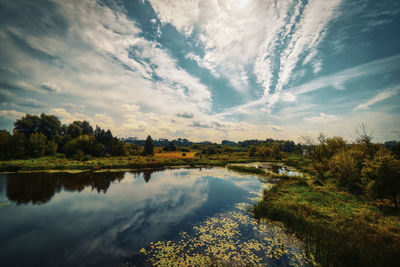 Scenic view of  river and meadow  against sky