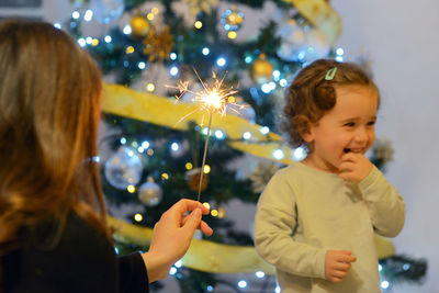 Woman holding illuminated sparkler against smiling girl