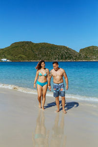 Full length of shirtless man at beach against clear blue sky