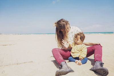 Woman sitting on beach by sea against sky