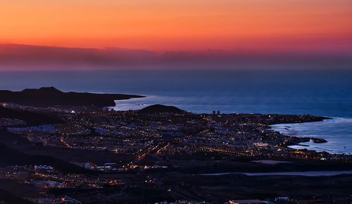 Aerial view of sea by buildings against sky during sunset