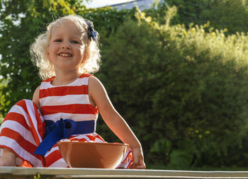 Pretty curly little girl seating in garden with plate of food and looking at the camera.