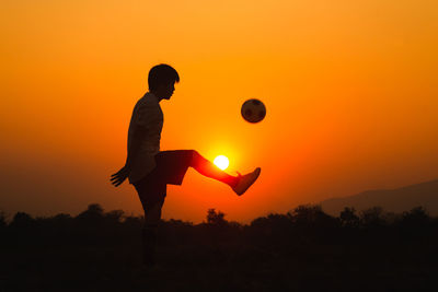 Silhouette man standing on field against orange sky