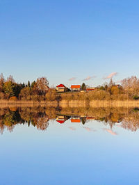 Reflection of tree and house in lake against sky