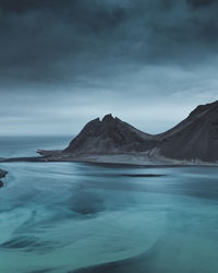 Scenic view of sea by mountains against sky