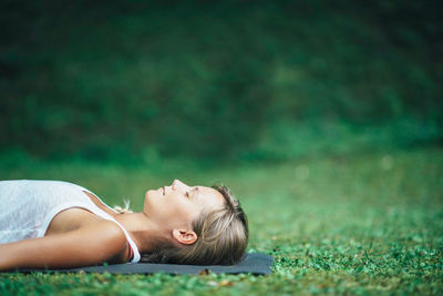 Side view of young woman practicing shavasana in park