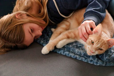 A young adolescent girl lying on a couch finds comfort by snuggling and petting her tabby cat