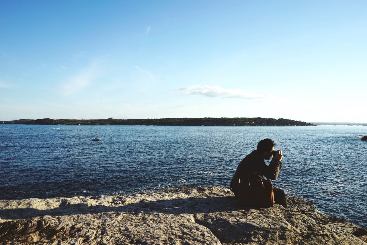 water, sea, leisure activity, lifestyles, sky, men, tranquility, tranquil scene, nature, scenics, beach, beauty in nature, shore, blue, sitting, standing, rear view, copy space