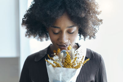 Young woman with eyes closed smelling flowers in front of wall