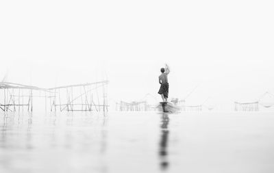 Rear view of man standing by lake against sky