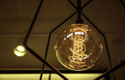 Low angle view of illuminated light bulb hanging from ceiling