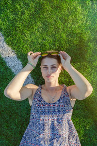 Girl in a dress lies on a green artificial field and looks up, vertical photo