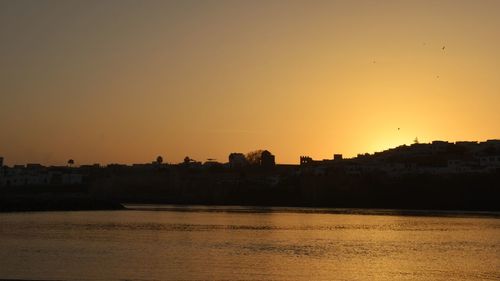 Buildings by river against romantic sky at sunset