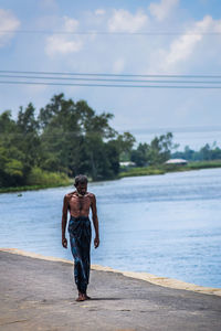 Full length of shirtless man walking by sea against sky