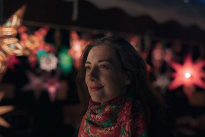 Close-up of thoughtful woman standing against illuminated lanterns at market during night