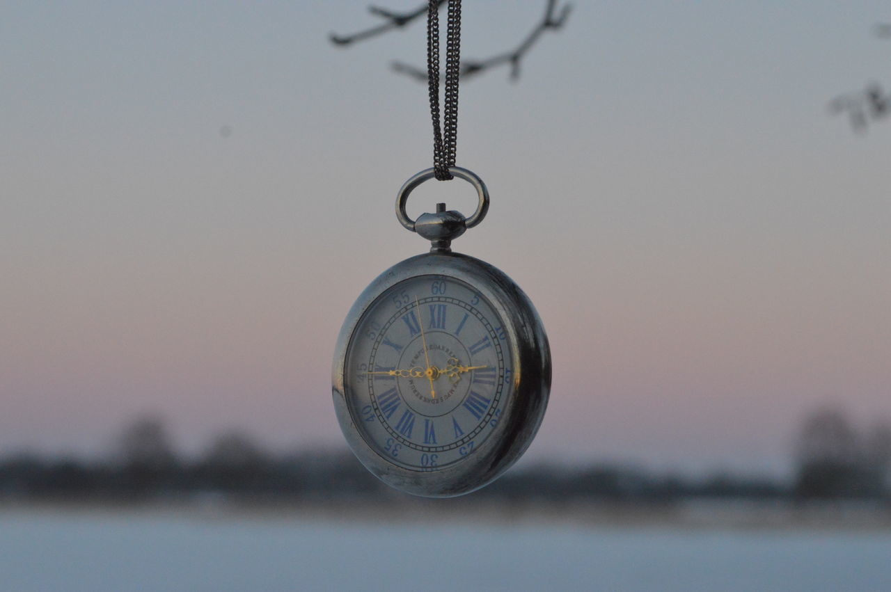 CLOSE-UP OF CLOCK HANGING ON METAL AGAINST SKY