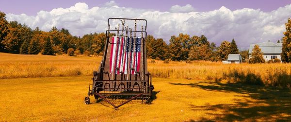 Empty bench on grassy field against cloudy sky