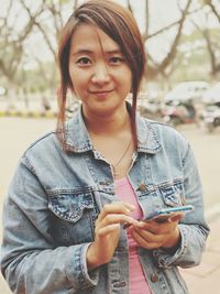 Portrait of young woman using mobile phone while standing outdoors