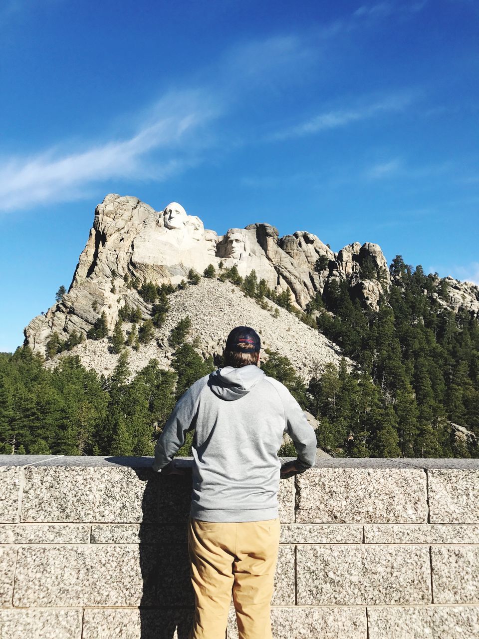 REAR VIEW OF MAN STANDING AGAINST MOUNTAINS