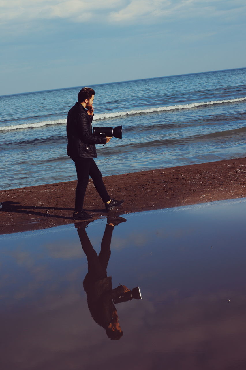 water, sea, real people, one person, full length, beach, sky, lifestyles, land, leisure activity, beauty in nature, horizon over water, casual clothing, horizon, nature, young adult, reflection, technology, wireless technology, outdoors