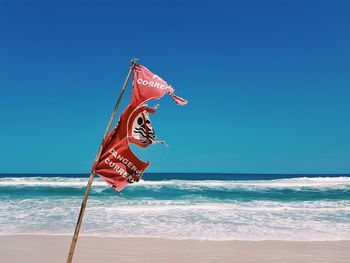 Torn flag at beach against clear blue sky