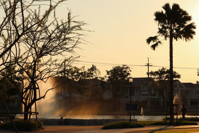 Silhouette trees by building against sky during sunset