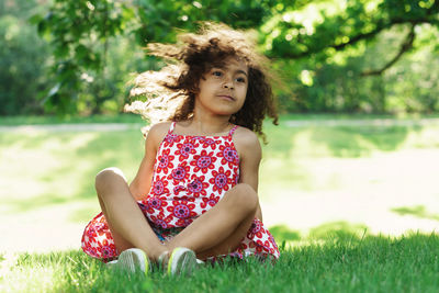 Girl looking away while sitting on grass at park