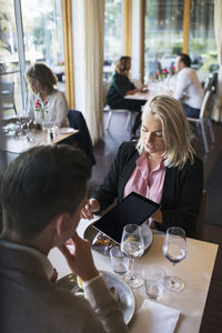 Businesswoman discussing with male colleague while showing digital tablet during meeting at restaurant