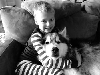 Portrait of cute boy sitting with dog on sofa at home