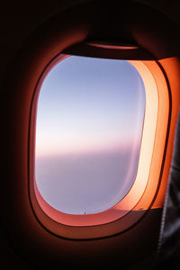 Through window of airplane flying over fluffy clouds in sunset blue sky