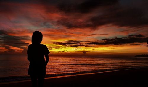 Silhouette man looking at sea against sky during sunset