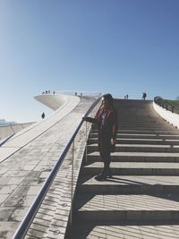 Rear view of woman walking on staircase against clear sky