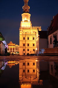 Reflection of illuminated poznan town hall in puddle at night