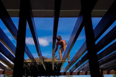 Low angle view of man standing on railing against sky
