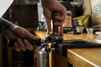 Cropped hands crushing coffee beans in portafilter at cafe