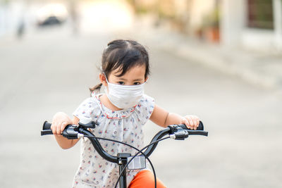 Little girl wearing medical mask prevent flu, pollutions and convid-19 riding bicycle outdoor.