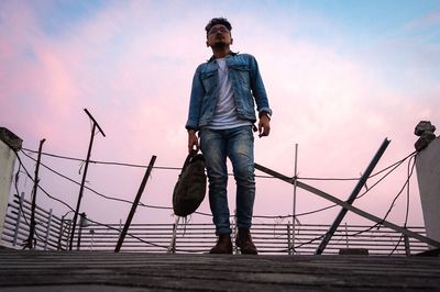 Man standing on railing against sky during sunset