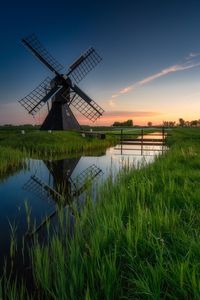 Traditional windmill on field against sky during sunset