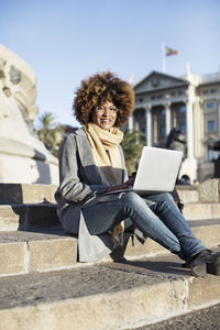 Portrait of smiling woman using laptop computer while sitting on steps