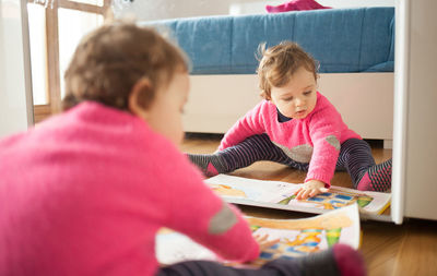 Cute girl looking at picture book while sitting by mirror at home