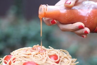 Cropped hand of woman pouring sauce on noodles