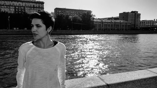 Thoughtful young woman standing against river in city