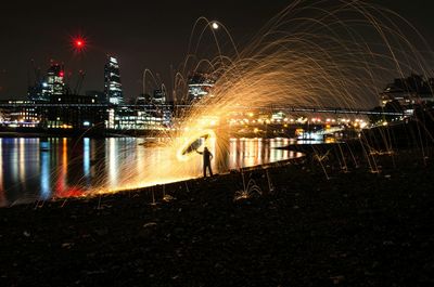 Silhouette person spinning wire wool by river in city at night