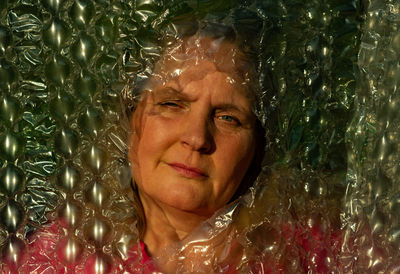 Portrait of a sad young woman face behind bubble wrap