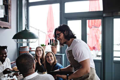 Smiling waiter talking to happy customers at restaurant