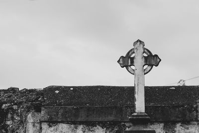 Low angle view of cross on wall against sky