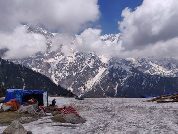 Man sitting by frozen lake against snowcapped mountains