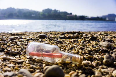 Message in a bottle on pebbles at beach against sky