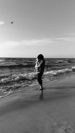 Mother carrying baby while standing on shore at beach against sky